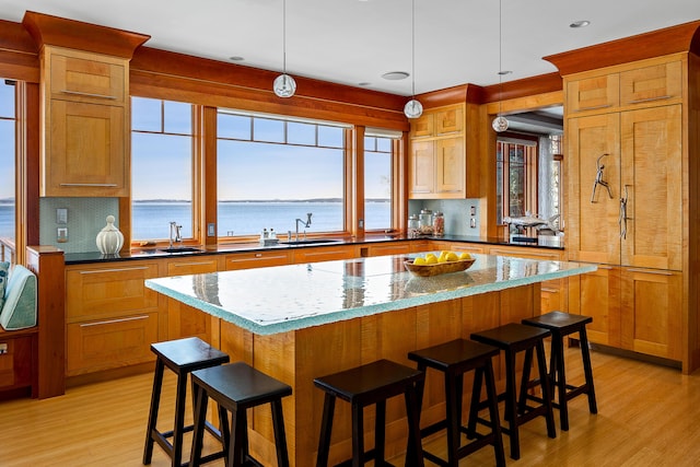 kitchen with tasteful backsplash, light wood-style flooring, a center island, a water view, and a sink