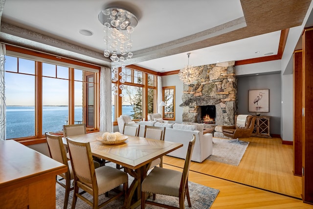 dining area featuring crown molding, light wood finished floors, a water view, an inviting chandelier, and a stone fireplace