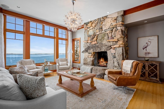 living area with a chandelier, a stone fireplace, a water view, and wood finished floors