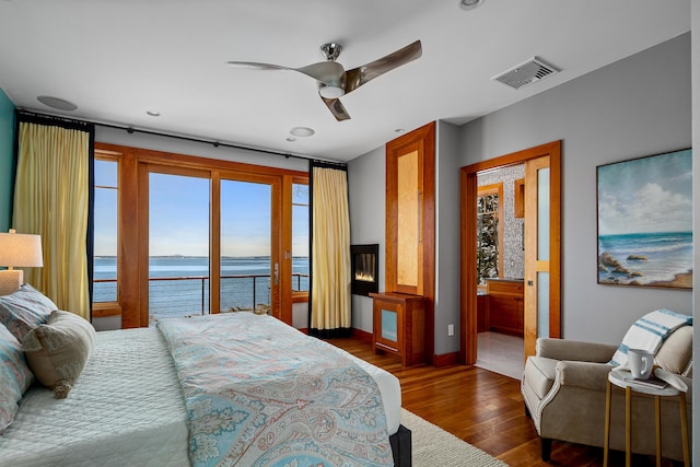 bedroom with wood finished floors, visible vents, a water view, and multiple windows