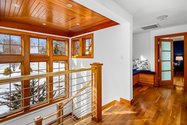 hall featuring wood finished floors, wood ceiling, an upstairs landing, visible vents, and baseboards