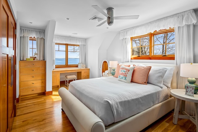 bedroom with ceiling fan, built in desk, light wood-style flooring, and visible vents