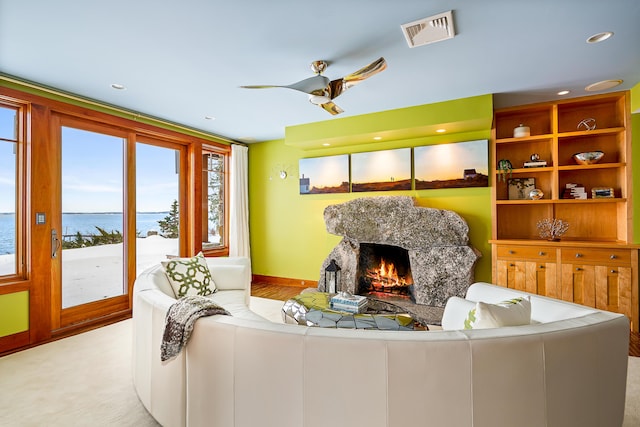 living room featuring a warm lit fireplace, visible vents, a ceiling fan, a water view, and recessed lighting