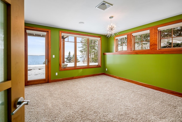 empty room with a notable chandelier, carpet floors, visible vents, and baseboards