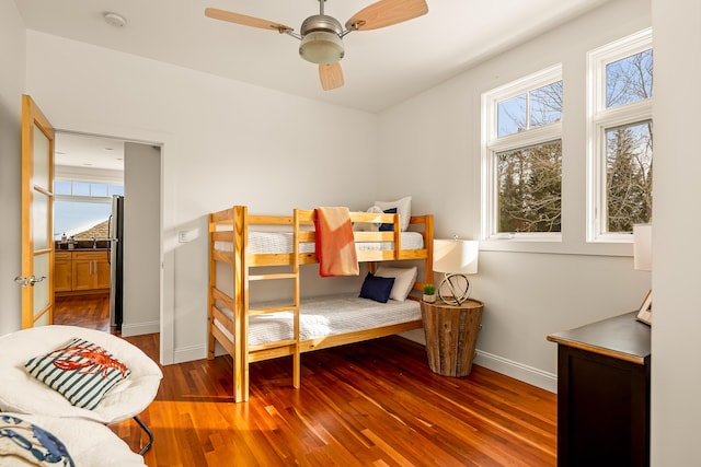 bedroom featuring multiple windows, wood finished floors, freestanding refrigerator, and baseboards