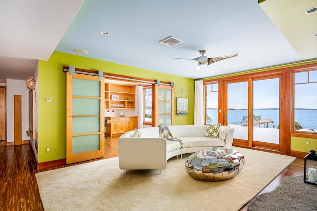 living area with visible vents, a water view, a barn door, a ceiling fan, and wood finished floors