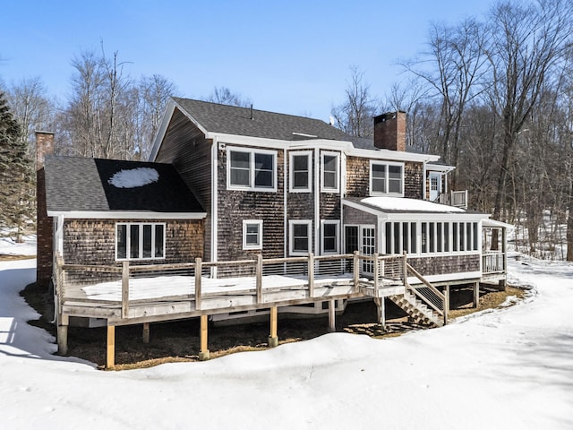 snow covered rear of property featuring a deck, roof with shingles, and a chimney