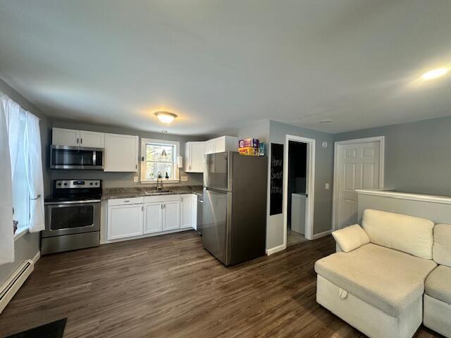 kitchen featuring dark countertops, baseboard heating, stainless steel appliances, white cabinetry, and a sink