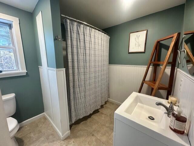 bathroom featuring toilet, a wainscoted wall, a sink, and a shower with shower curtain