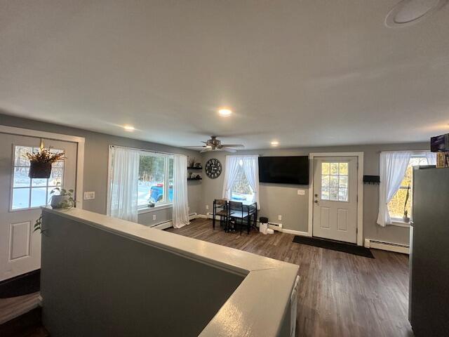 living area featuring a baseboard heating unit, a wealth of natural light, dark wood-style flooring, and a ceiling fan