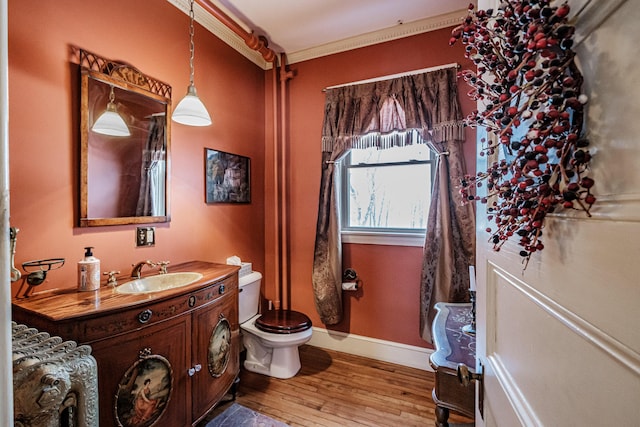 bathroom featuring toilet, wood finished floors, vanity, baseboards, and crown molding