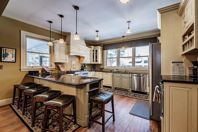 kitchen featuring glass insert cabinets, appliances with stainless steel finishes, a breakfast bar area, pendant lighting, and a sink