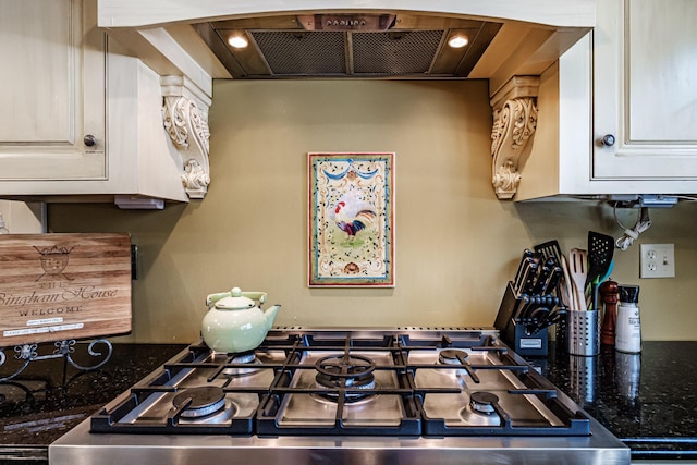 kitchen featuring dark stone counters, white cabinetry, wall chimney range hood, and stove