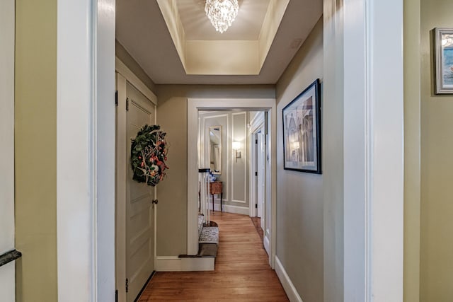 hallway with a tray ceiling, a notable chandelier, baseboards, and wood finished floors