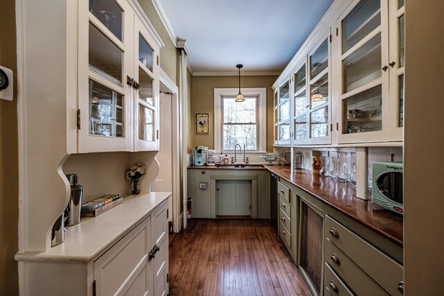 kitchen featuring a sink, white cabinets, hanging light fixtures, ornamental molding, and glass insert cabinets