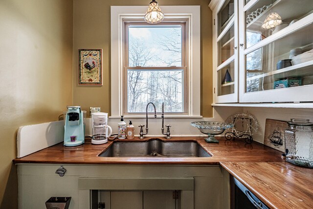 kitchen with pendant lighting, a wealth of natural light, glass insert cabinets, a sink, and butcher block countertops