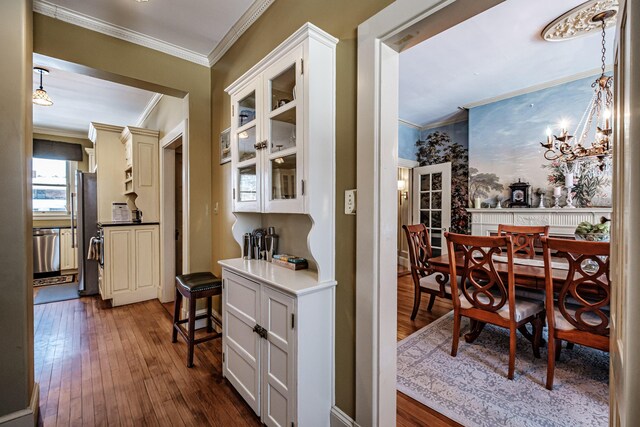 hall with an inviting chandelier, ornamental molding, and dark wood finished floors