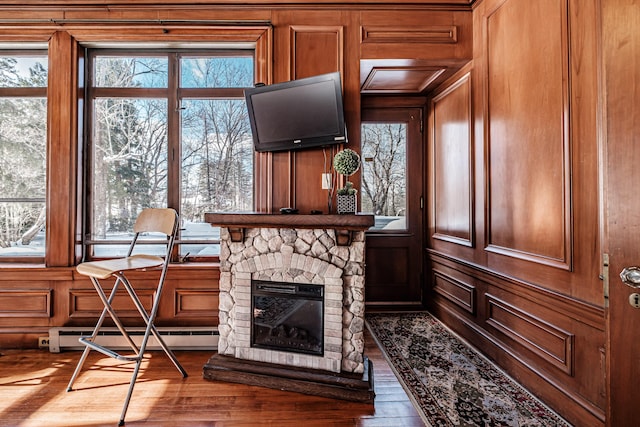 living area with wooden walls, a baseboard radiator, a stone fireplace, and wood finished floors