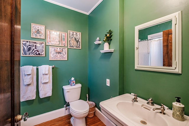 bathroom featuring crown molding, toilet, a sink, wood finished floors, and baseboards