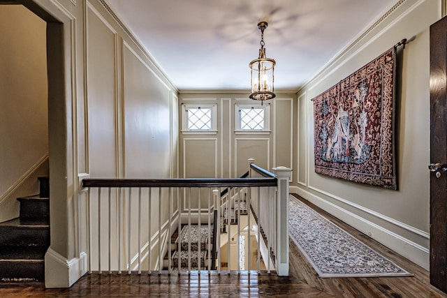 stairs with a notable chandelier, a decorative wall, crown molding, and wood finished floors