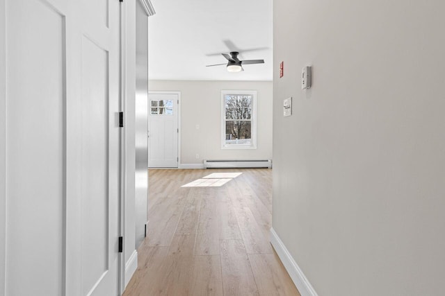 hallway with a baseboard radiator, baseboards, and light wood-style flooring