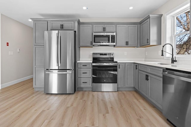 kitchen featuring gray cabinets, appliances with stainless steel finishes, light wood-style flooring, and a sink