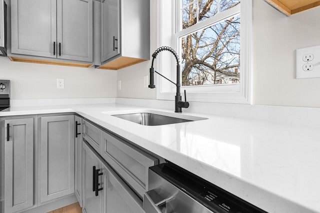 kitchen featuring a sink, stainless steel dishwasher, gray cabinetry, and light countertops