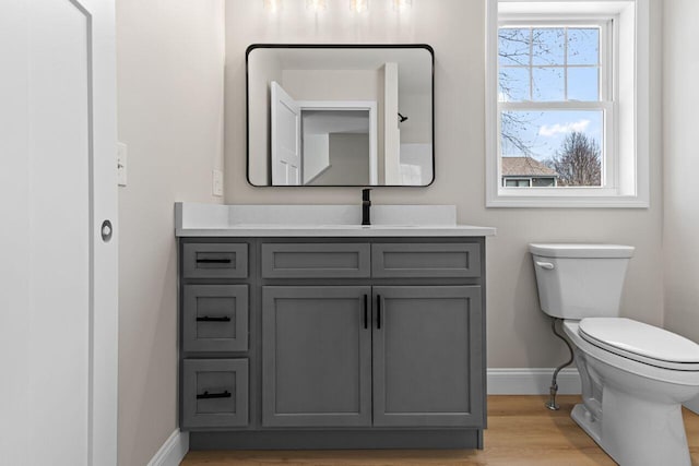 half bath featuring toilet, vanity, baseboards, and wood finished floors