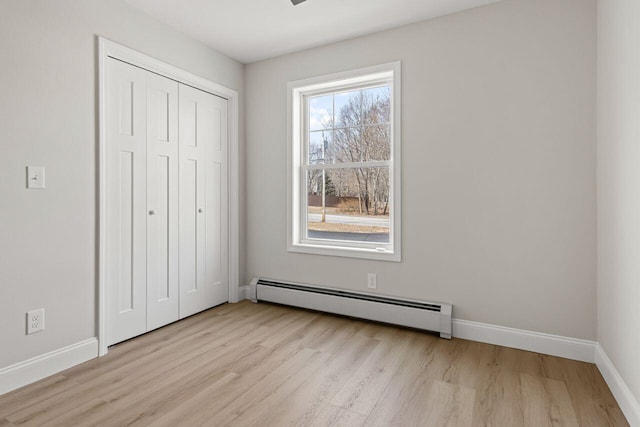 unfurnished bedroom with a closet, baseboard heating, baseboards, and wood finished floors