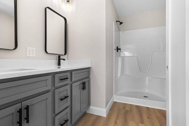 bathroom featuring a sink, wood finished floors, double vanity, baseboards, and walk in shower