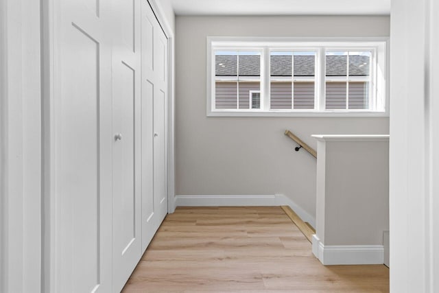 hall featuring light wood-style floors, baseboards, and a wealth of natural light