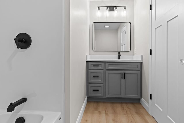 bathroom with vanity, a bathing tub, wood finished floors, and baseboards