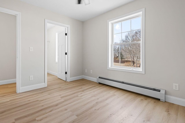 empty room with light wood finished floors, a baseboard heating unit, and baseboards