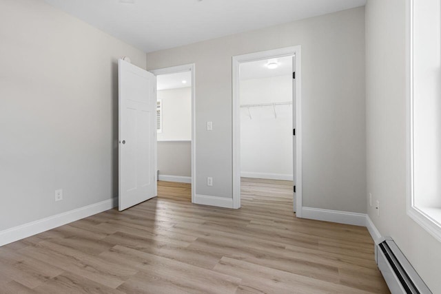 unfurnished bedroom with a walk in closet, baseboards, light wood-type flooring, and baseboard heating