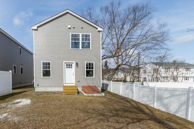 back of property with entry steps, fence, and a lawn