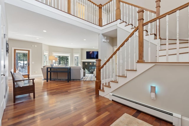 foyer entrance with baseboards, a glass covered fireplace, stairway, wood finished floors, and baseboard heating