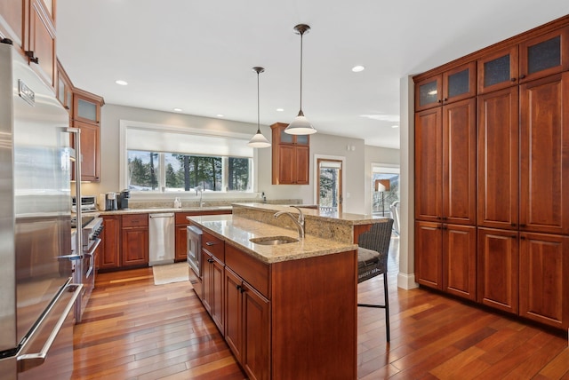 kitchen featuring glass insert cabinets, stainless steel appliances, a breakfast bar, a sink, and a center island with sink