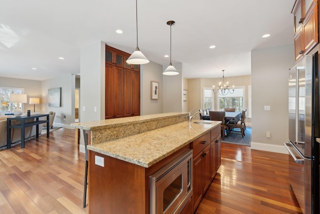 kitchen featuring stainless steel appliances, hanging light fixtures, brown cabinetry, and glass insert cabinets