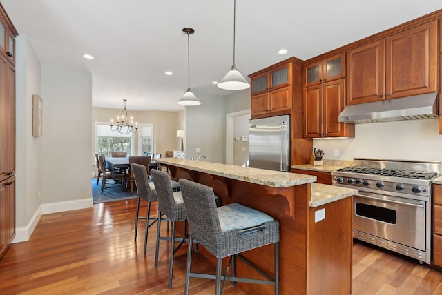 kitchen with under cabinet range hood, glass insert cabinets, pendant lighting, and premium appliances