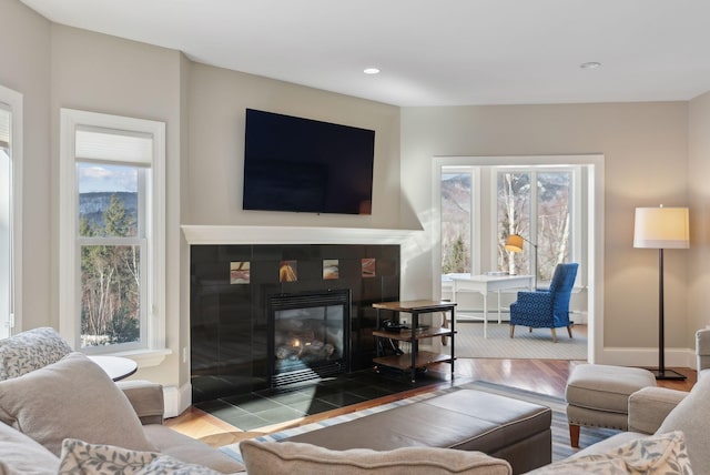 living area featuring recessed lighting, baseboard heating, wood finished floors, a tile fireplace, and baseboards