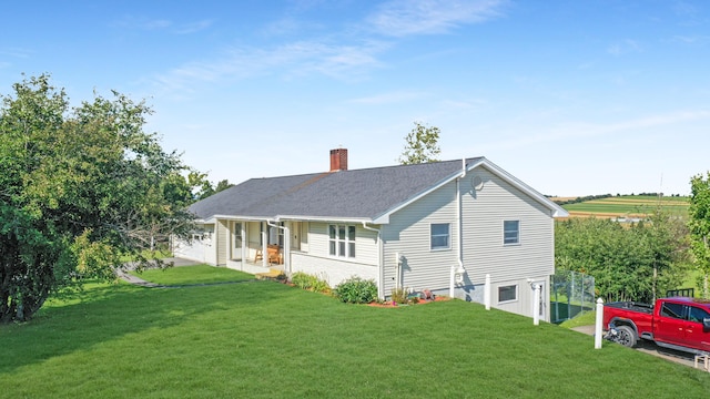 back of house featuring a shingled roof, covered porch, a lawn, and a chimney