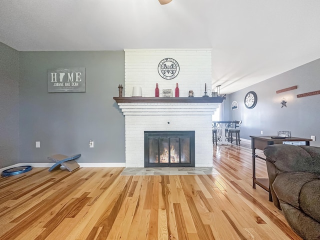 living room with a brick fireplace, baseboards, and wood finished floors