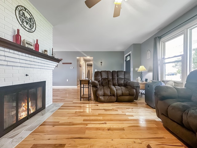 living area featuring light wood-style flooring, a fireplace, baseboards, and a ceiling fan