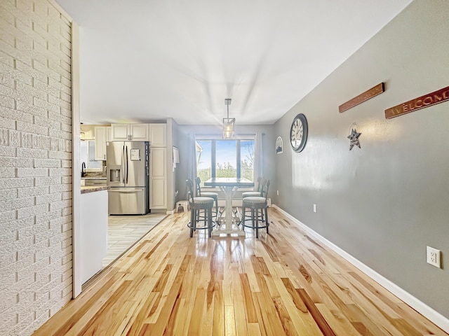 unfurnished dining area featuring brick wall, a sink, light wood-style flooring, and baseboards