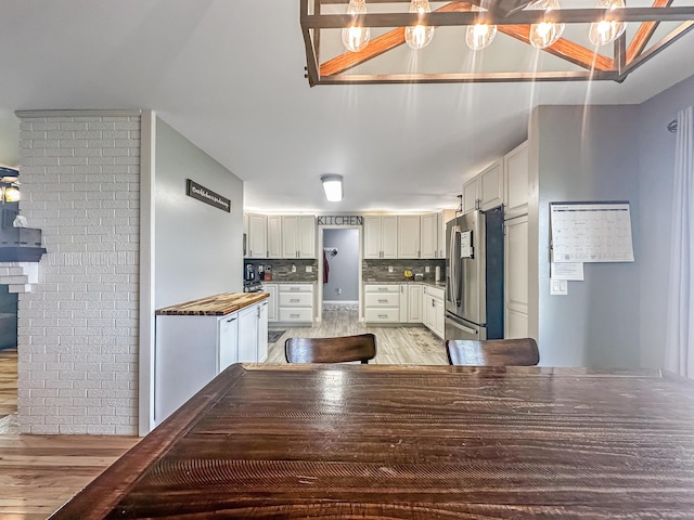 kitchen featuring backsplash, freestanding refrigerator, white cabinetry, brick wall, and light wood-type flooring