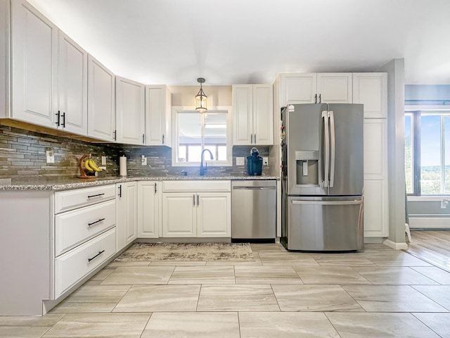 kitchen featuring light stone counters, a sink, white cabinets, appliances with stainless steel finishes, and pendant lighting