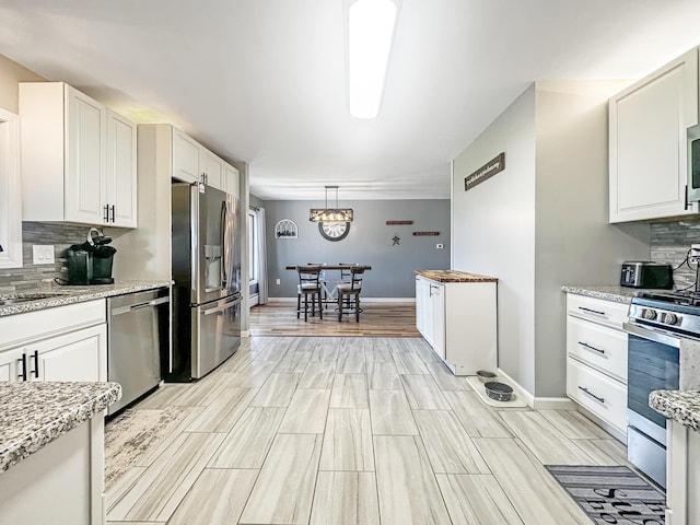 kitchen with appliances with stainless steel finishes, pendant lighting, white cabinets, and light stone countertops