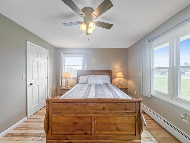 bedroom with baseboards, baseboard heating, a ceiling fan, and light wood-style floors