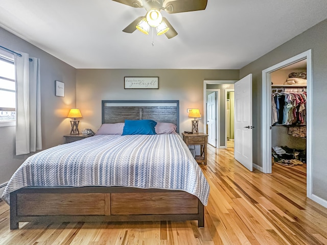 bedroom with a walk in closet, a closet, a ceiling fan, wood finished floors, and baseboards