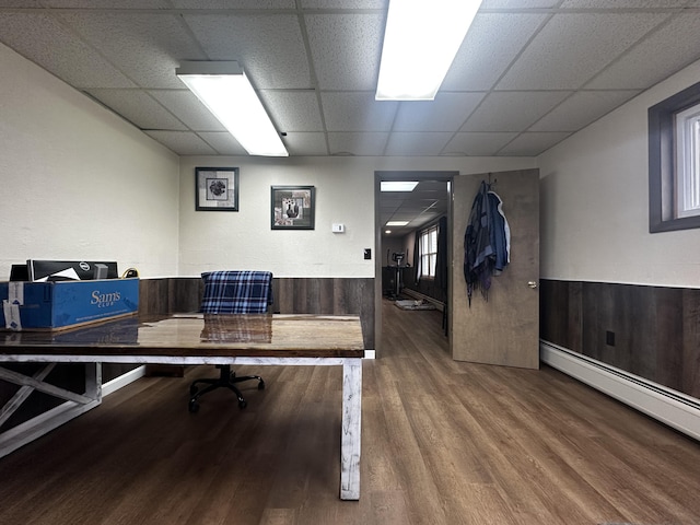 home office with a baseboard radiator, a wainscoted wall, a drop ceiling, and wood finished floors